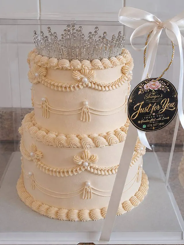 Two-tier ivory celebration cake with piped pearl detailing and a crystal tiara