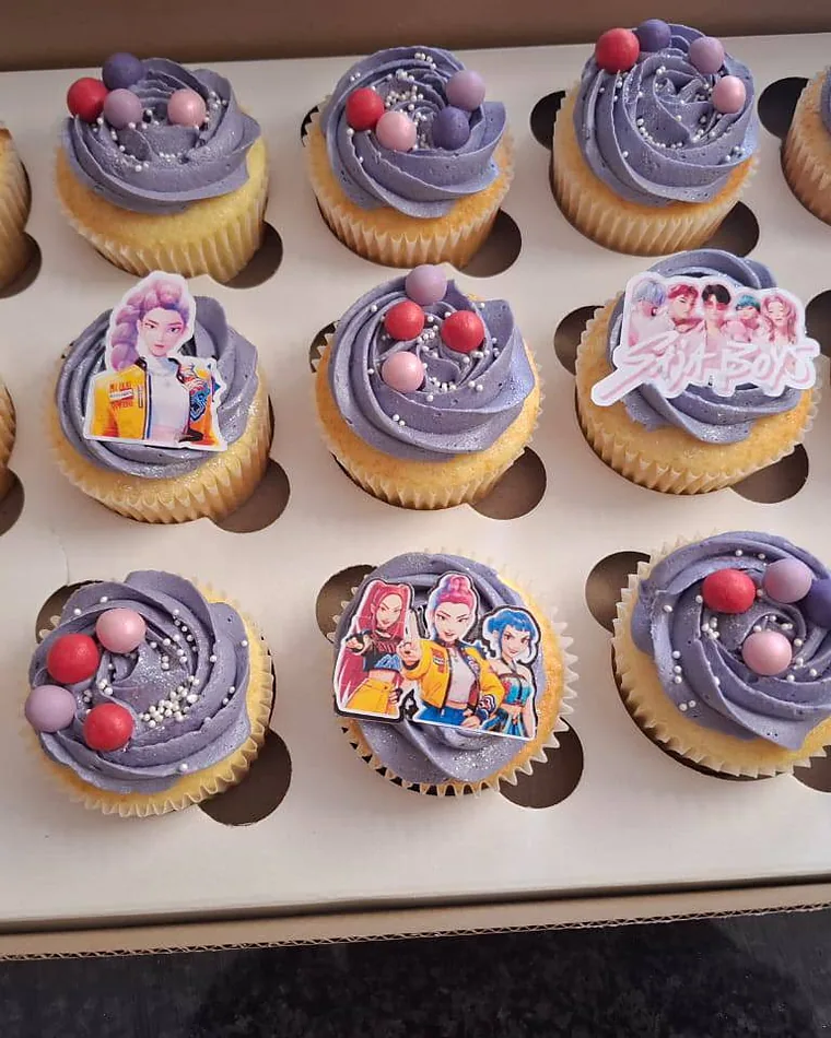 A box of themed cupcakes with lilac swirls, sugar pearls and printed character toppers