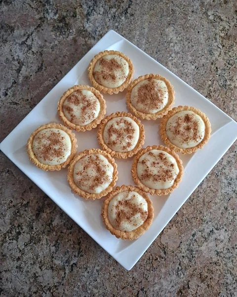 Nine milk tart tartlets dusted with cinnamon on a white platter